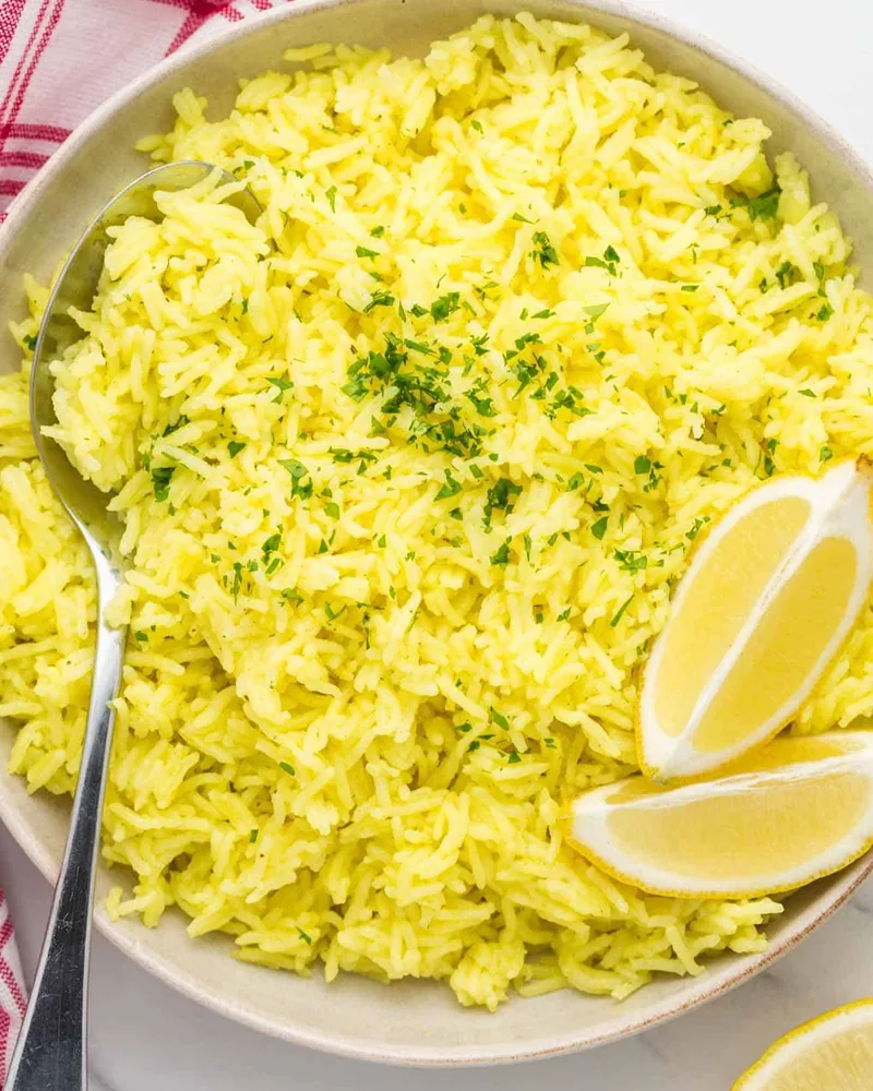 Yellow turmeric rice in a bowl with lemon wedges at Al Mecca