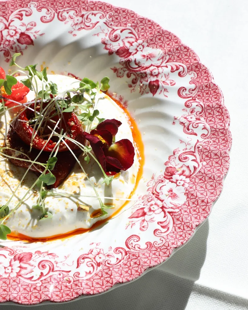 Burrata dish with microgreens and dried tomatoes on decorative ceramic plate at Ambrosiano
