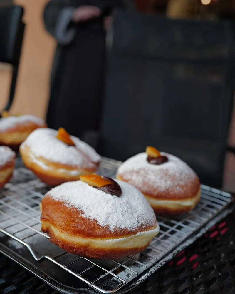 Sufganiyot pastries with powdered sugar and orange peel on a cooling rack at Ashkara Falafel