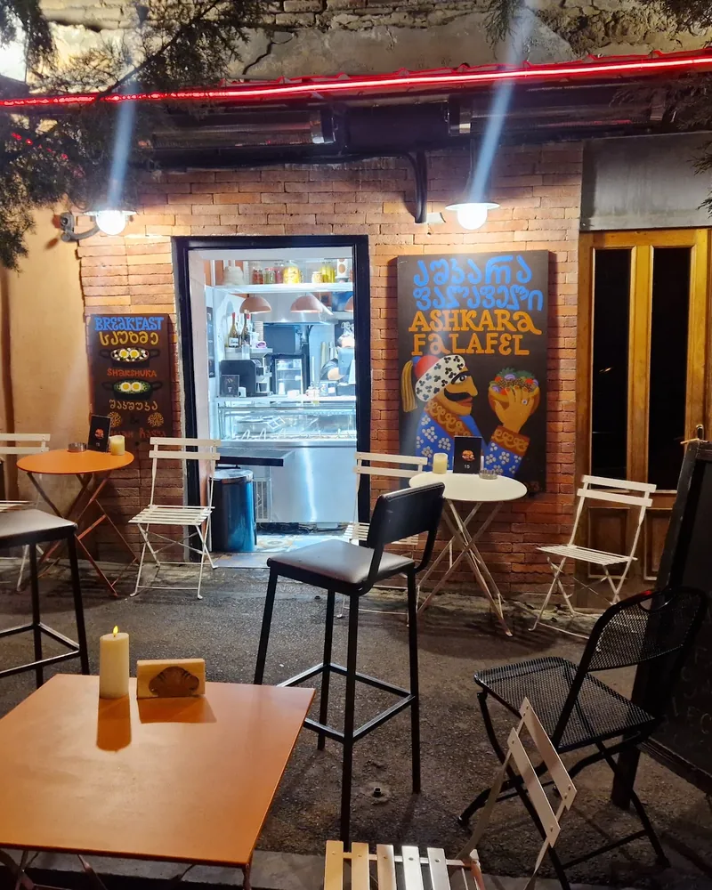 Outdoor patio seating and brick facade at night at Ashkara Falafel