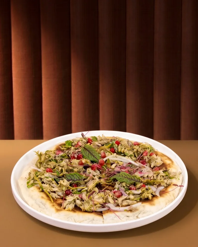 Flatbread topped with shredded meat, pomegranate seeds and greens at Asi Khinkali