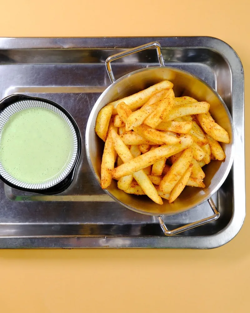 Seasoned french fries in a metal bowl with green dipping sauce at Aut Vera
