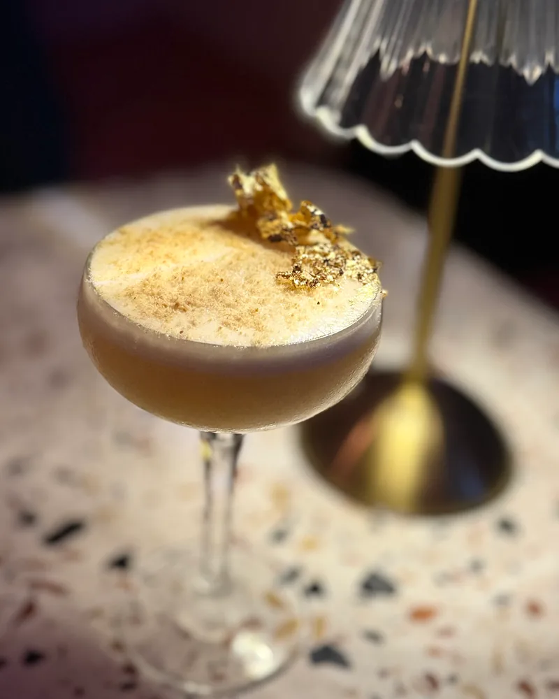 Cocktail in a coupe glass garnished with gold leaf at Barbar'a