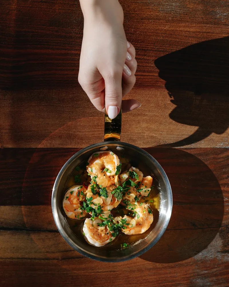 Garlic shrimp in a small skillet held by a hand at Barbatus