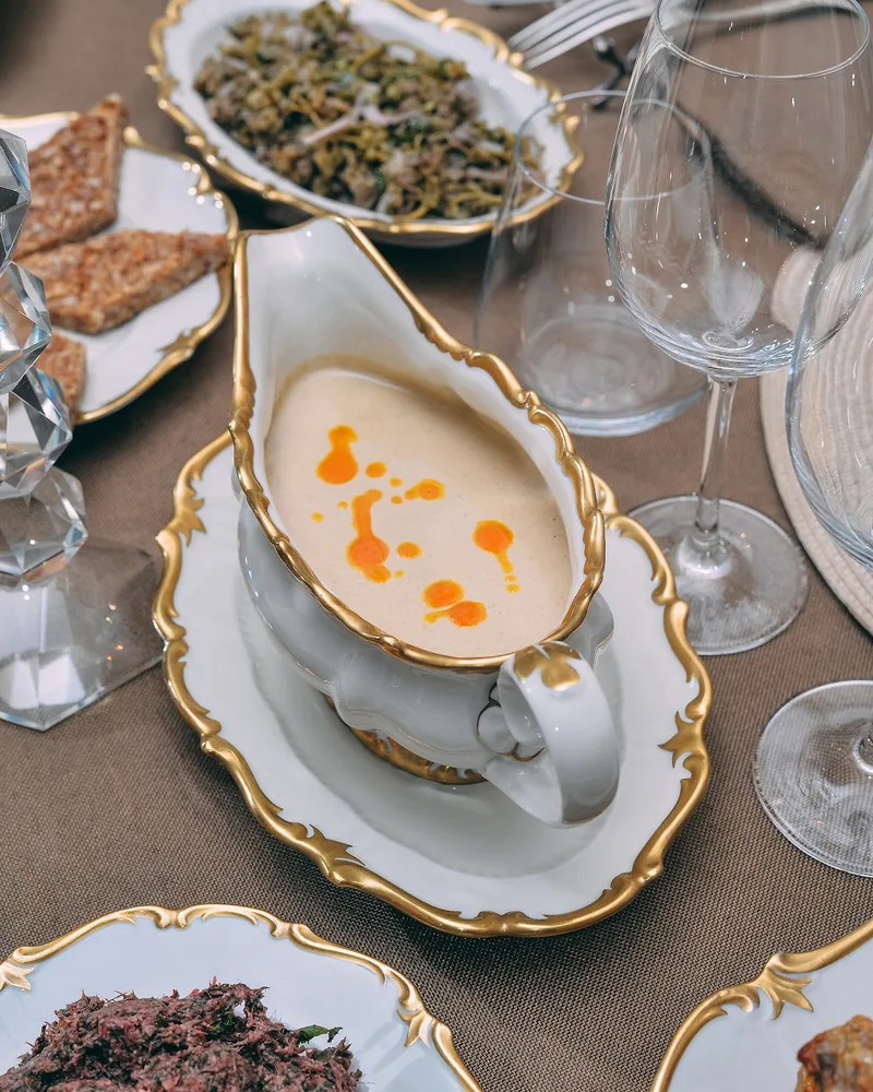 Pale walnut sauce with drops of orange oil in a gilded porcelain gravy boat on a set table