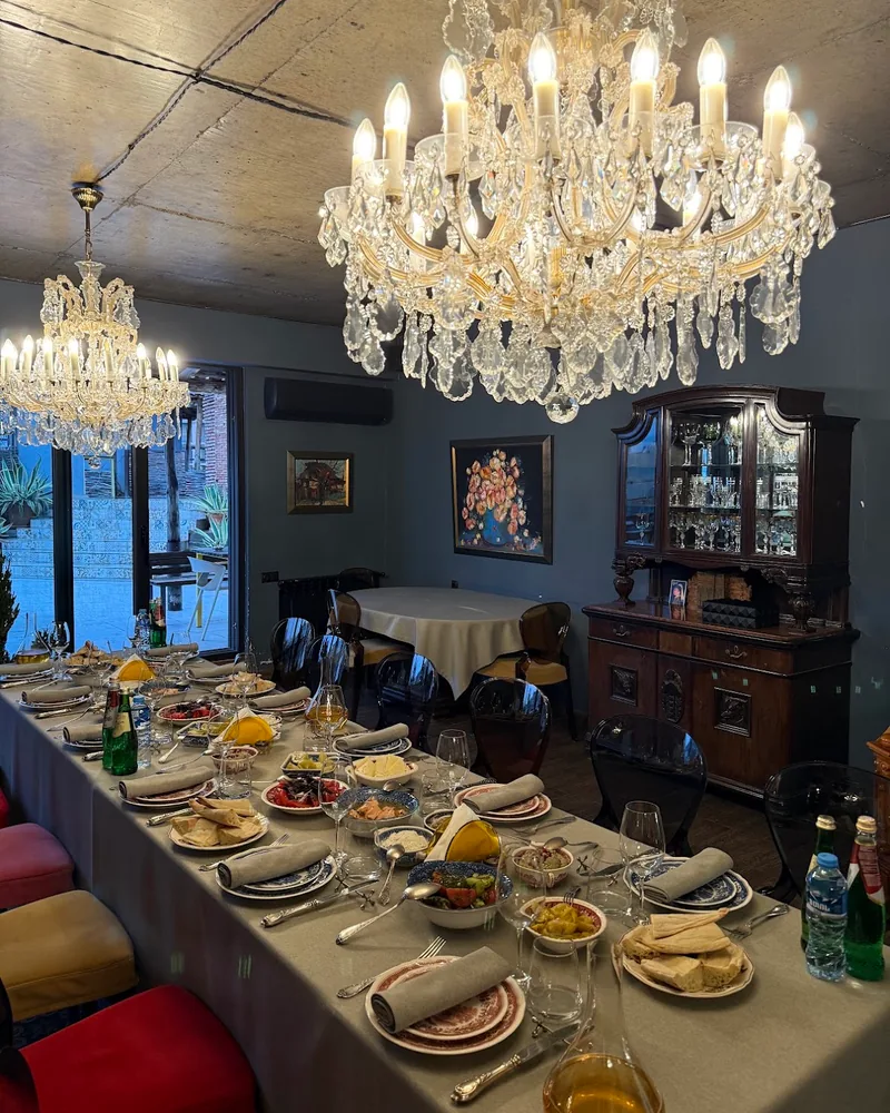 A long table laid with small plates of salads, cheese and bread, folded napkins and wine glasses under 2 crystal chandeliers at Bina N37