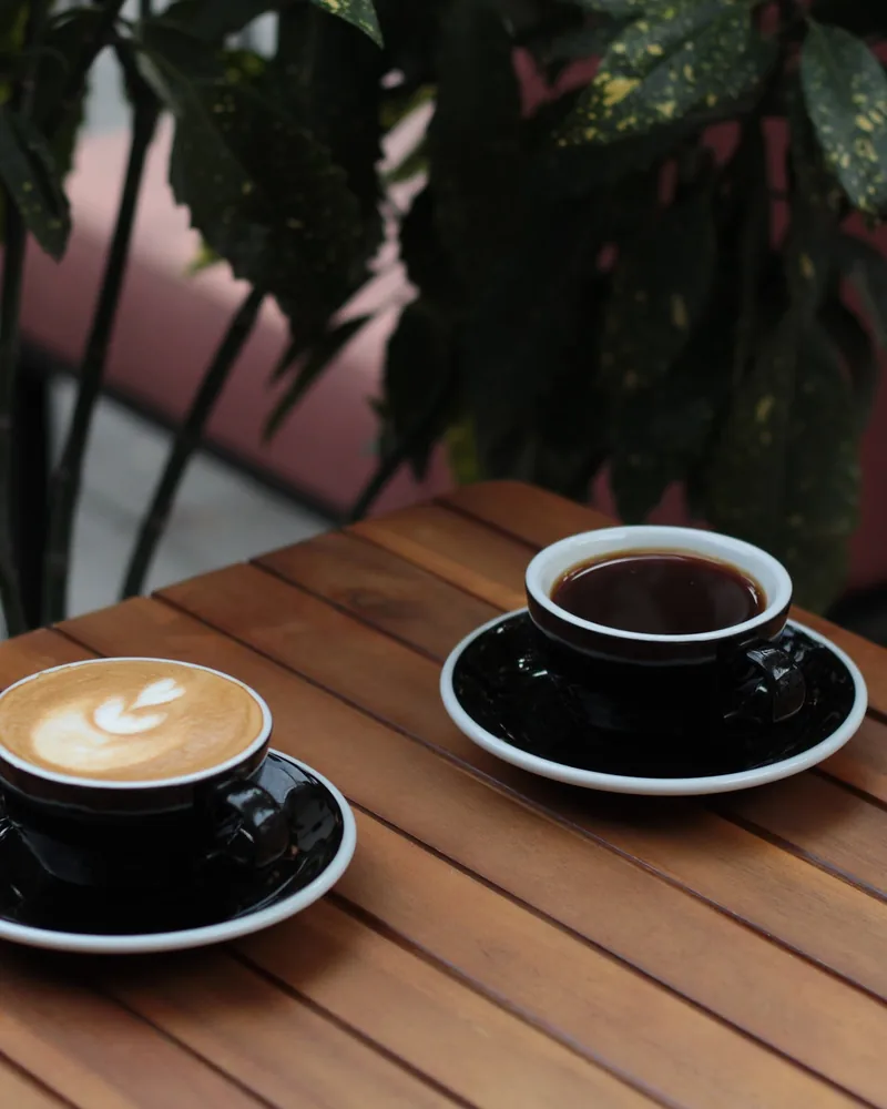 Cappuccino with latte art and black coffee on wooden slatted table at Black Cup
