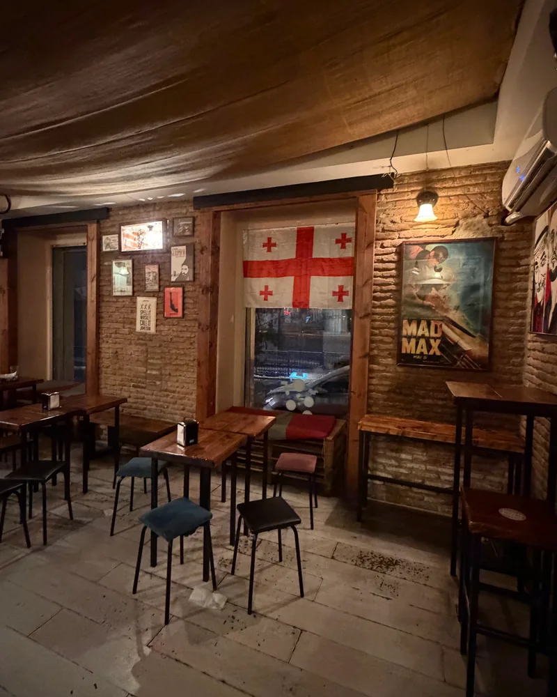 Brick-walled bar seating with posters and a Georgian flag at Black Dog Bar