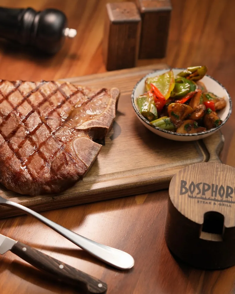 Grilled t-bone steak on a wooden board with sauces and side vegetables at Bosphorus Steakhouse & Terrace