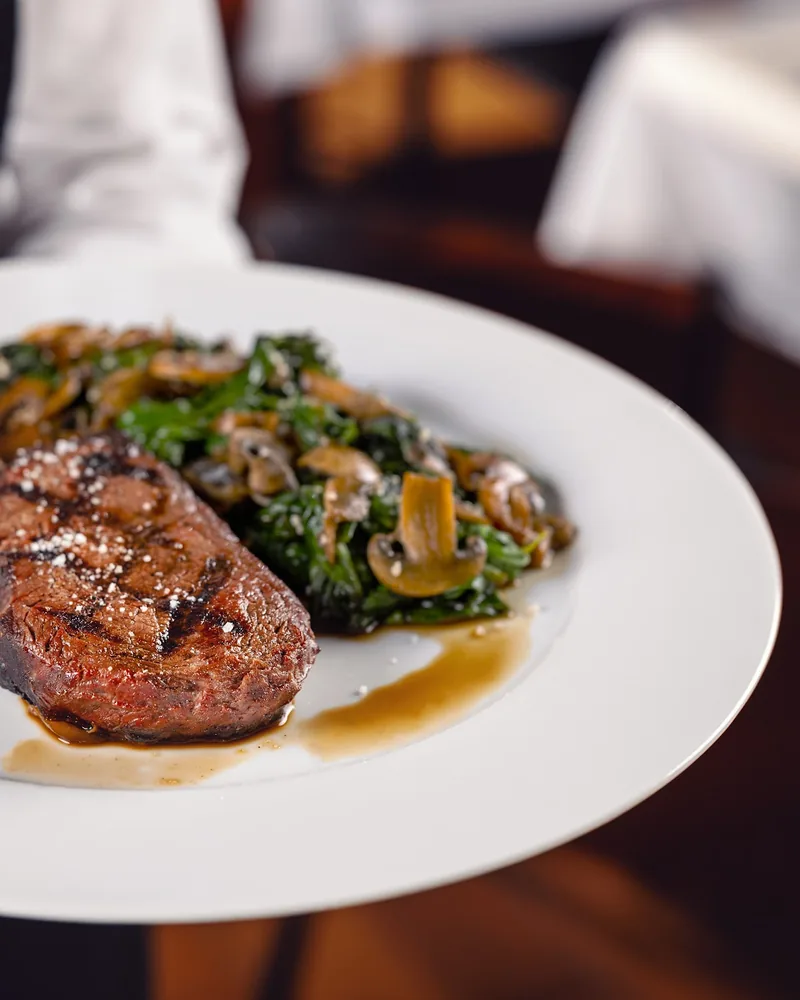 Steak with mushrooms and spinach on a white plate at Brasserie Buvette