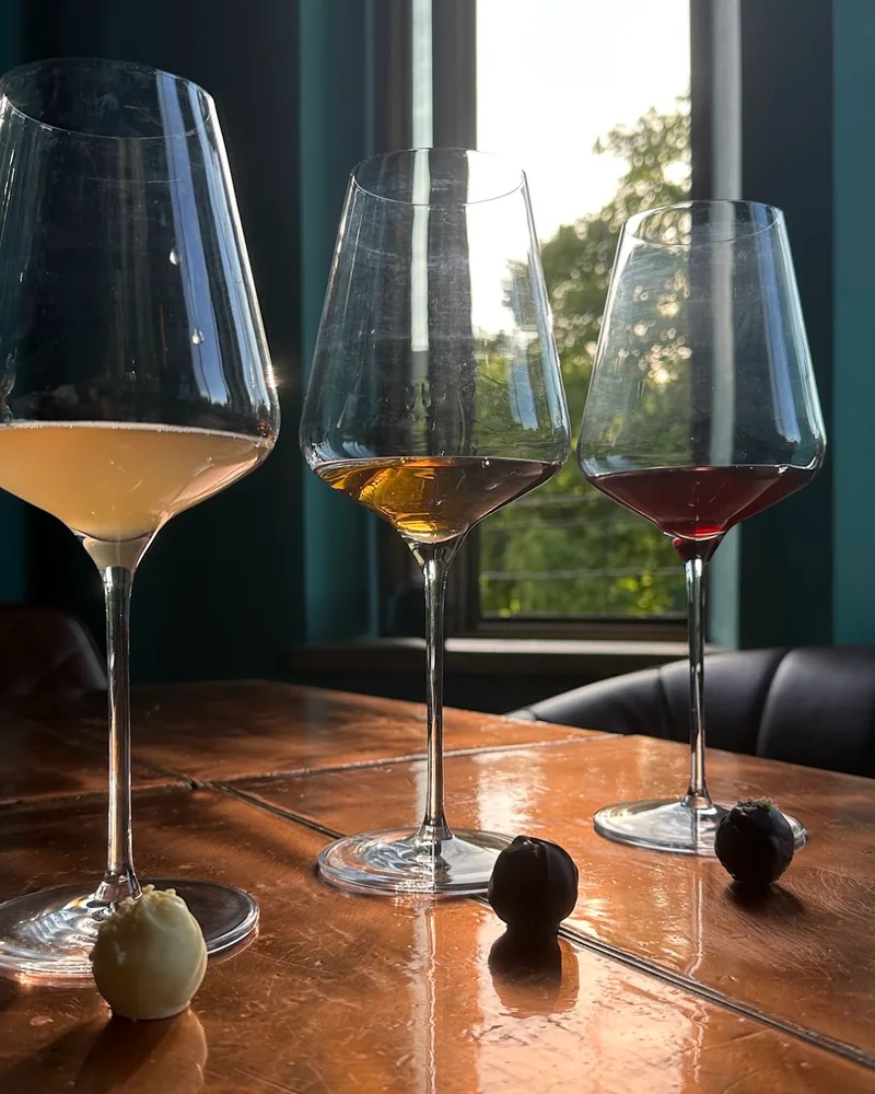 3 glasses of wine, pale, amber and red, with chocolate truffles on a copper table by a window at Bu & Khari