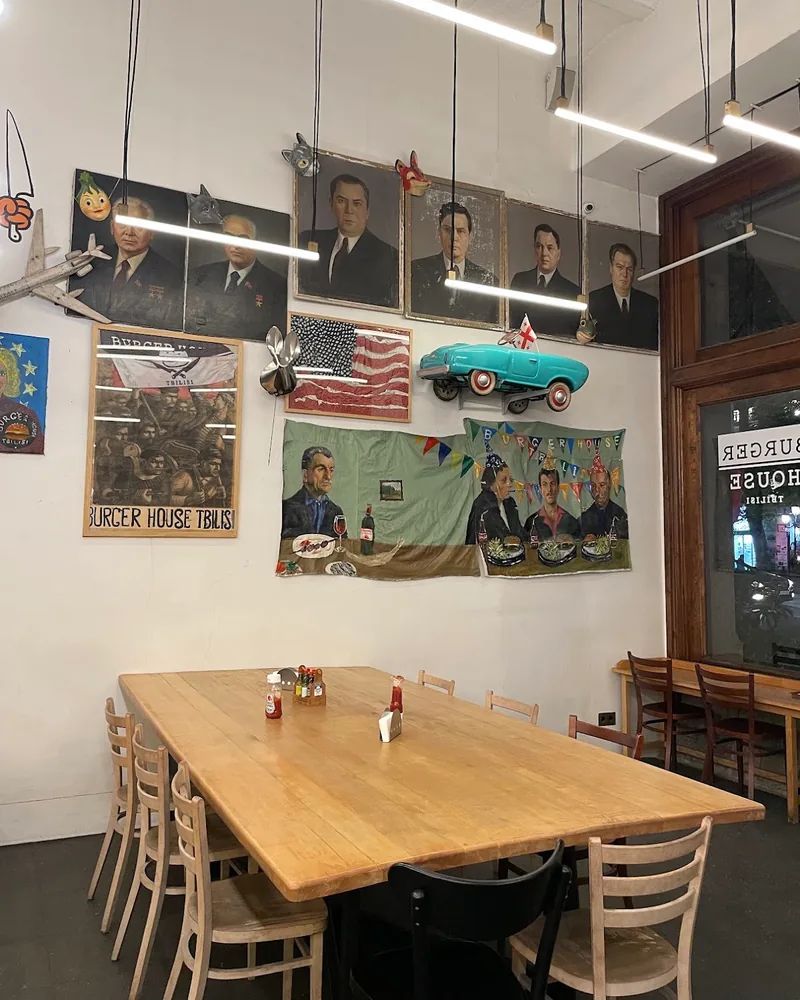 Dining area with wooden communal table and quirky wall art at Burger House