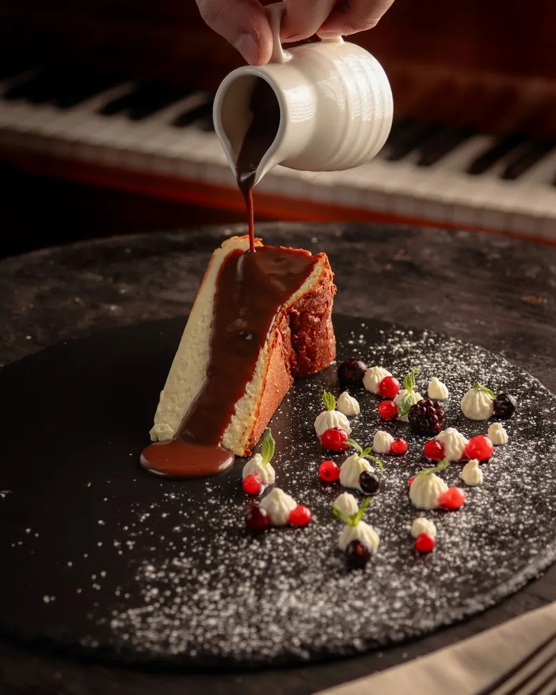Cheesecake slice with chocolate sauce poured over it and berries at Cafe Dante