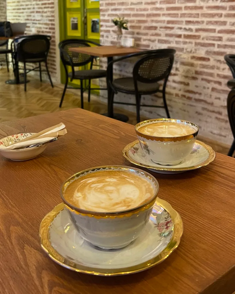 2 cappuccinos with latte art in gold-rimmed vintage porcelain cups on a wooden table at Cafe Mellow