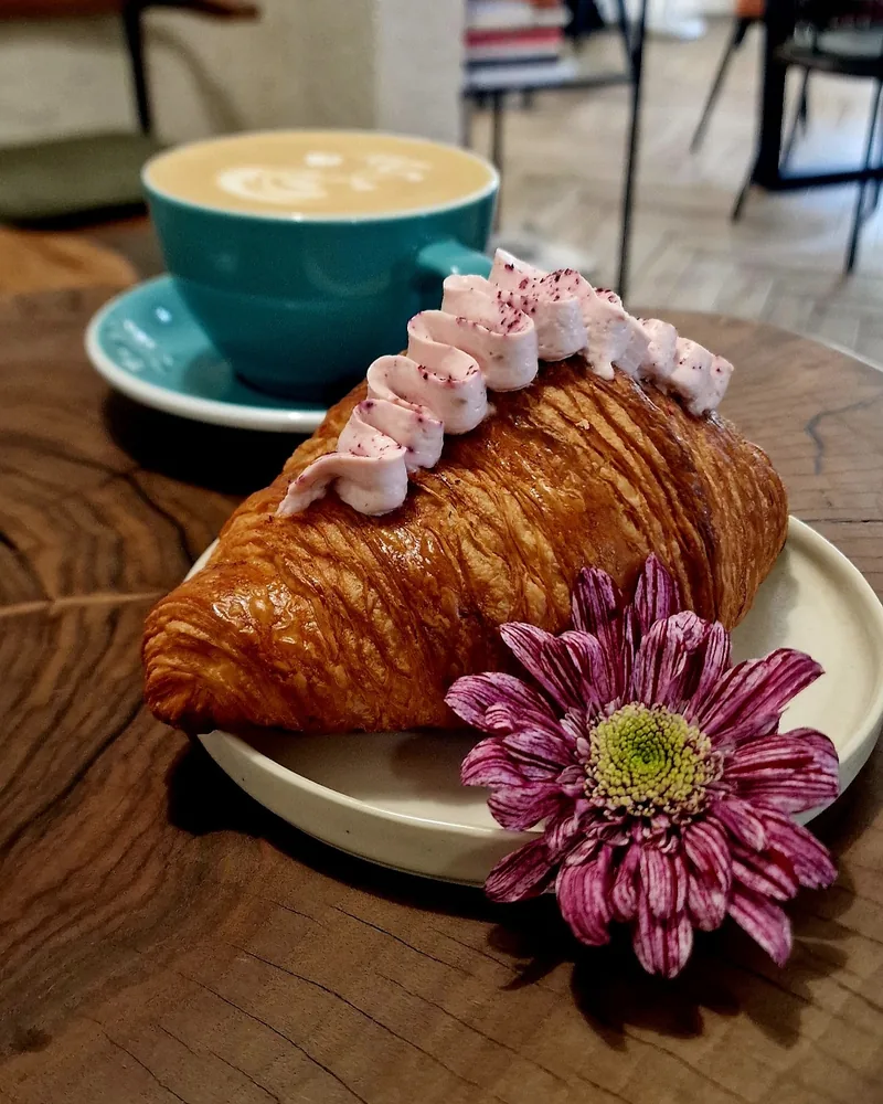 Croissant with pink cream garnish and purple flower at Caffeine by WorkIn