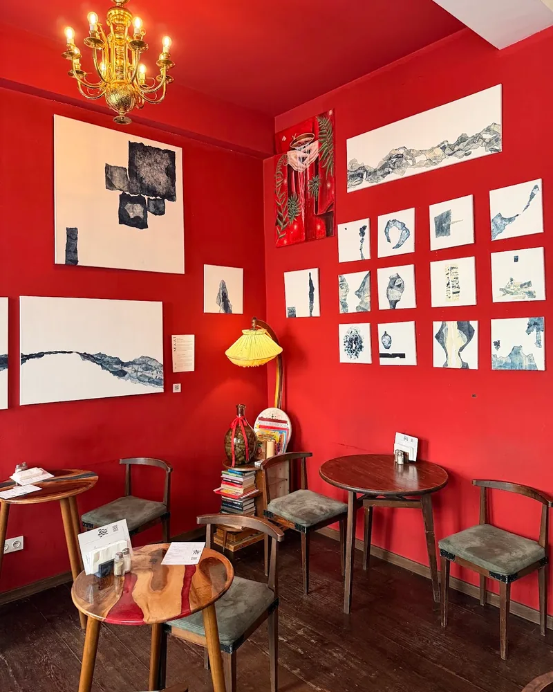Red room with art-covered walls and wooden tables at Chaduna