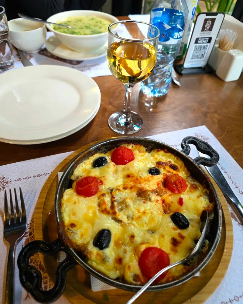 Baked dish with melted cheese, tomatoes, and olives in a cast iron skillet at Chashnagiri