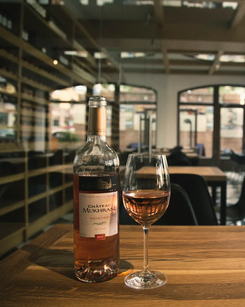 Rosé wine bottle and glass on a wooden table at Château Mukhrani Wine Bar