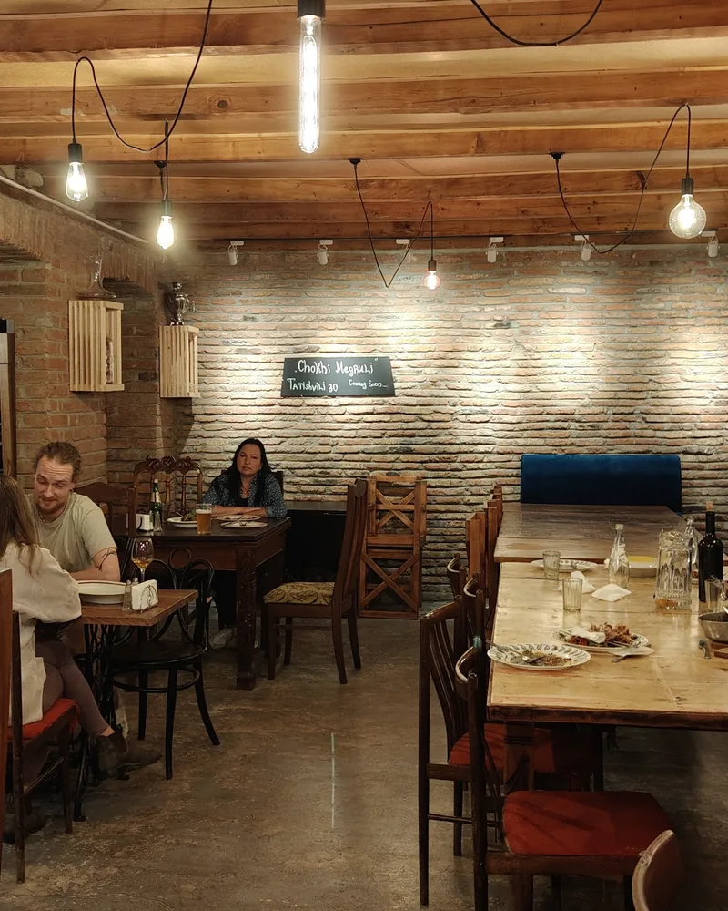 Brick-walled dining room with wooden beams and tables at Chokhi Veraze