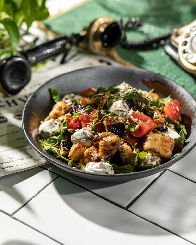 Fried eggplant salad with tomatoes and creamy dressing in a dark bowl at Chveni