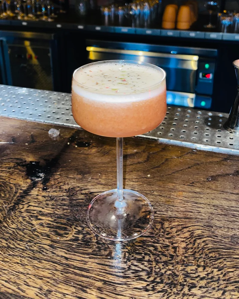 Frothy cocktail in a coupe on a wooden bar at Cocktail Factory
