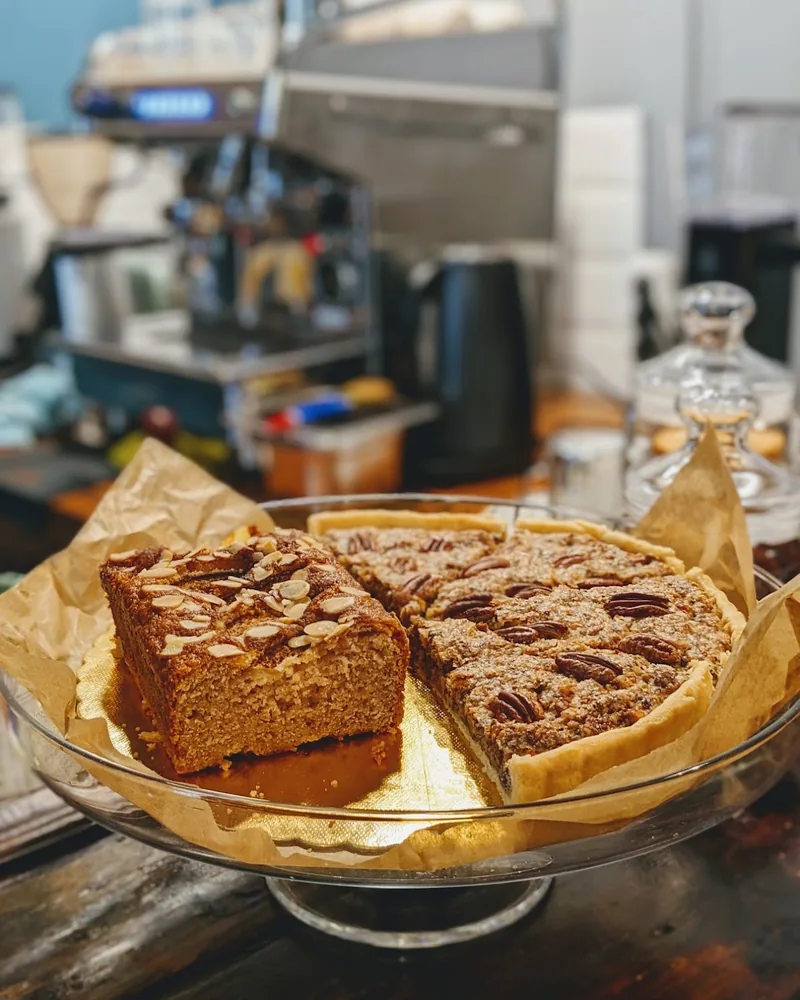 Almond cake slice and pecan tart on a glass cake stand at Coffee Place