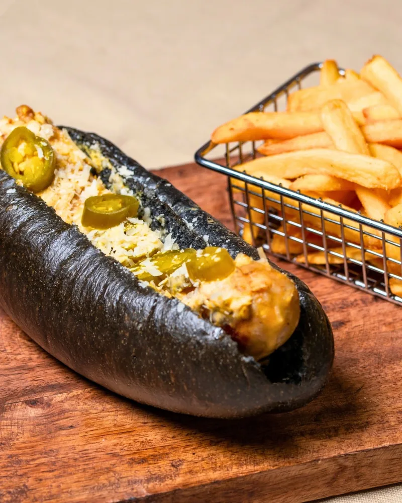 Hot dog in a black bun with jalapeños and french fries at Craft Food