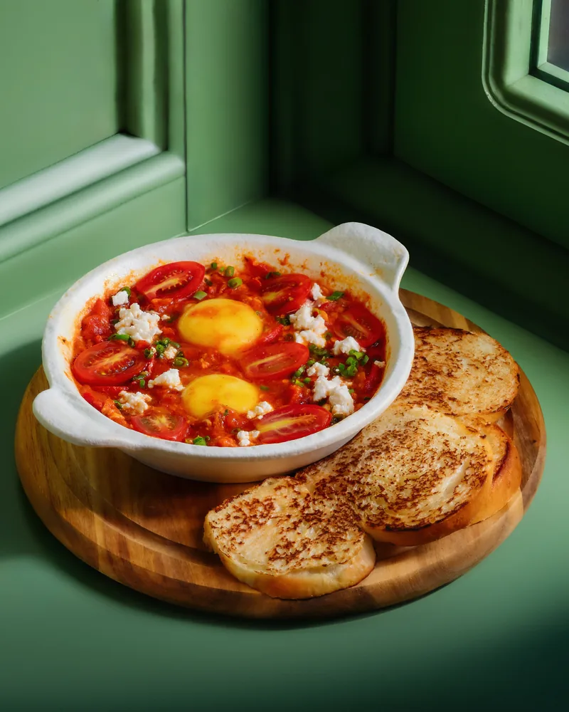 Shakshuka in a white dish with toasted bread on a wooden board at Crossroads Bistro