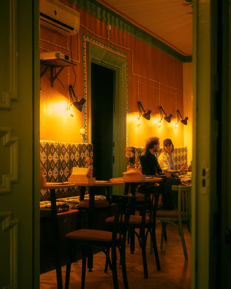 Dining room with a patterned banquette and wall lamps seen through a green door at Crossroads Bistro