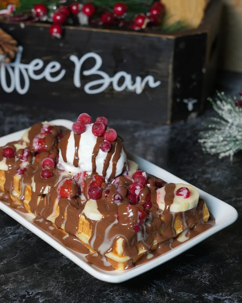 Waffle topped with ice cream, chocolate sauce, banana, and berries at Daily Dose