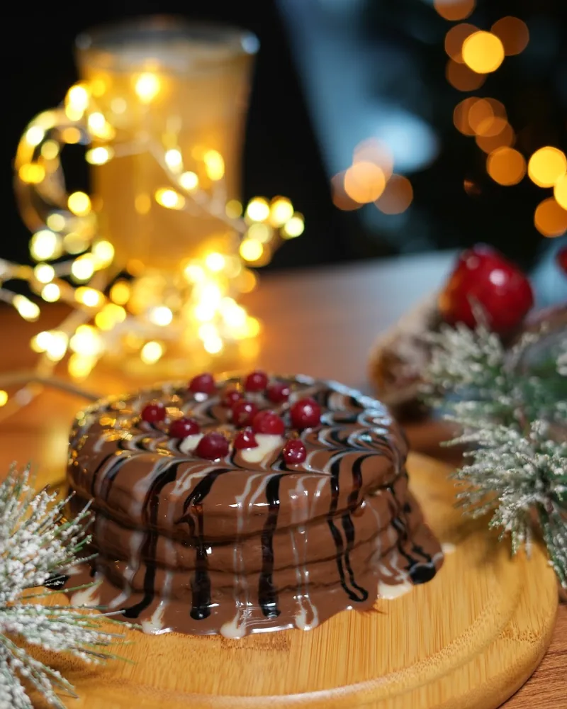 Stack of chocolate-glazed pancakes with berries on a wooden board at Daily Dose