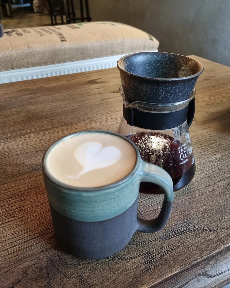 Latte with heart latte art in a ceramic mug and pour over coffee server at Daily Grind
