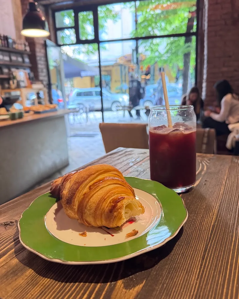 Croissant on a green rimmed plate with an iced drink at Daily Grind