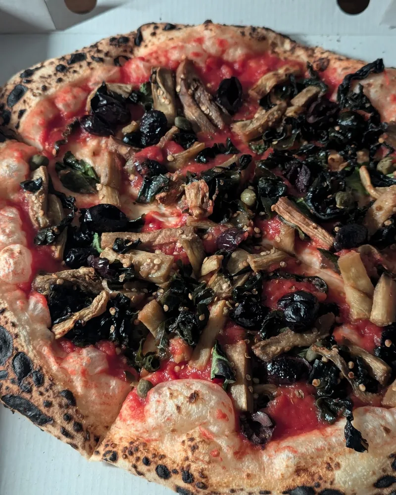Neapolitan pizza with eggplant, greens, and olives in a cardboard box at Daner Pizza