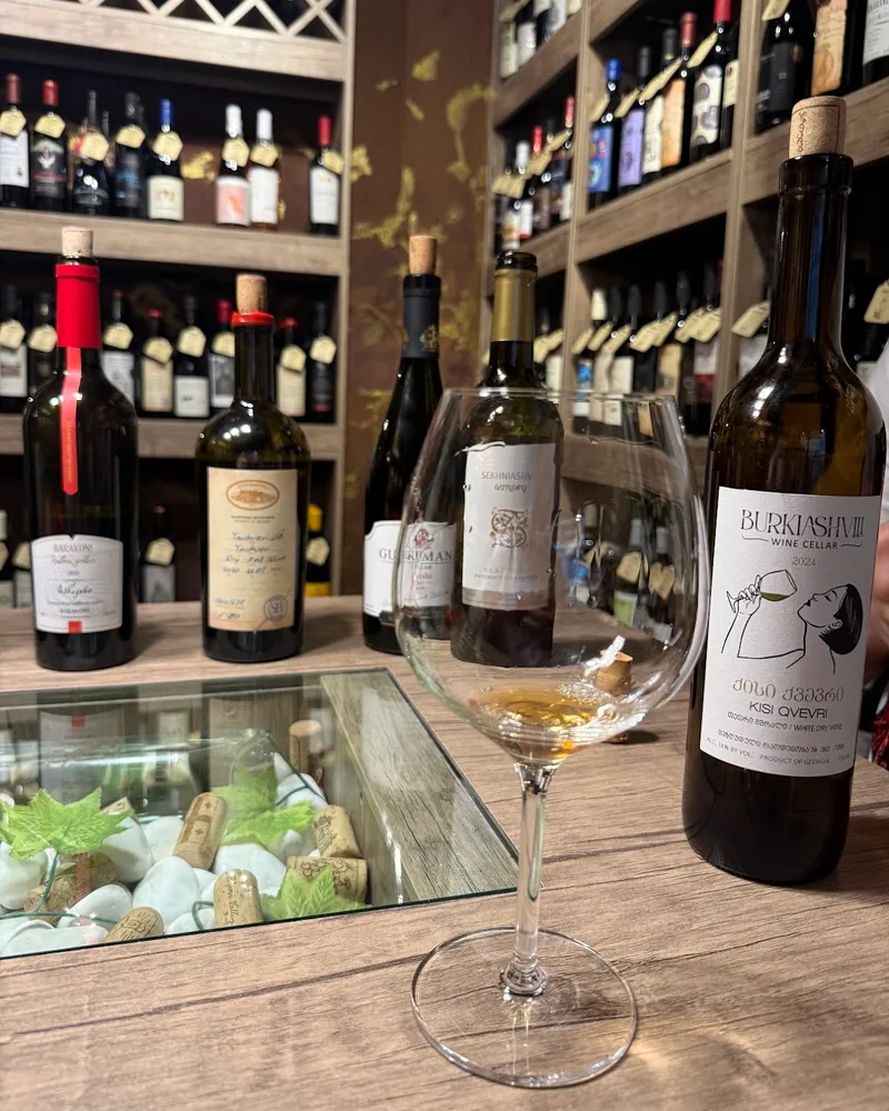 Amber wine tasting in a glass with bottles at Dionysus Wine Shop
