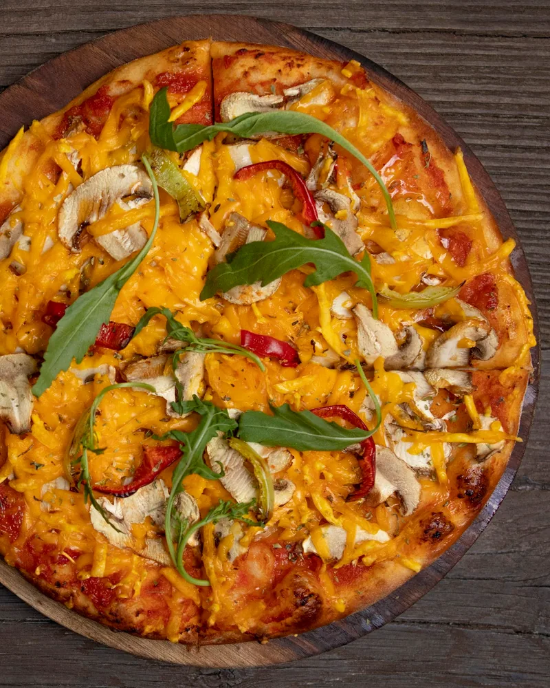 Vegan pizza with mushrooms, peppers and rocket on a wooden board at Doomfara