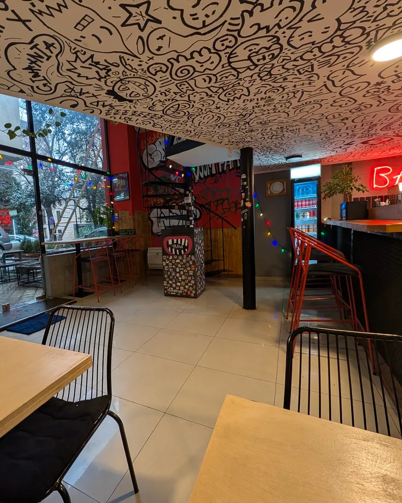 Cafe room with a doodled ceiling, red bar stools and a neon bar sign at Doomfara