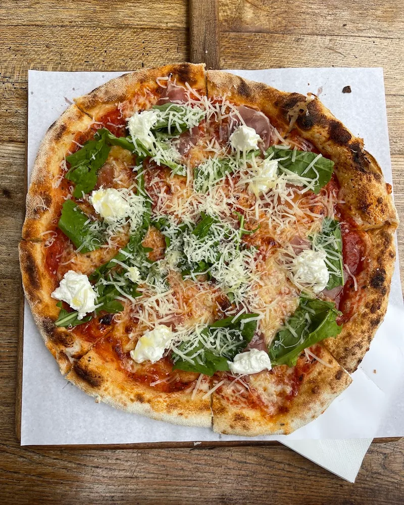 Pizza with burrata, prosciutto, and greens on a wooden peel at Farina