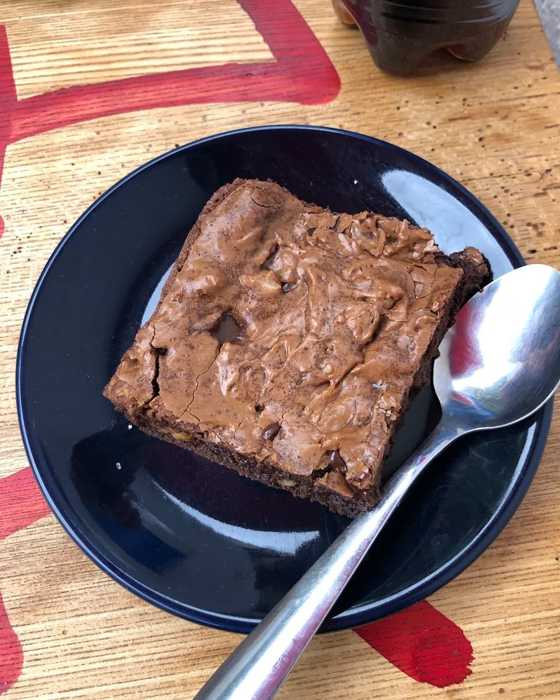 Chocolate brownie on a black plate with a spoon at Farina