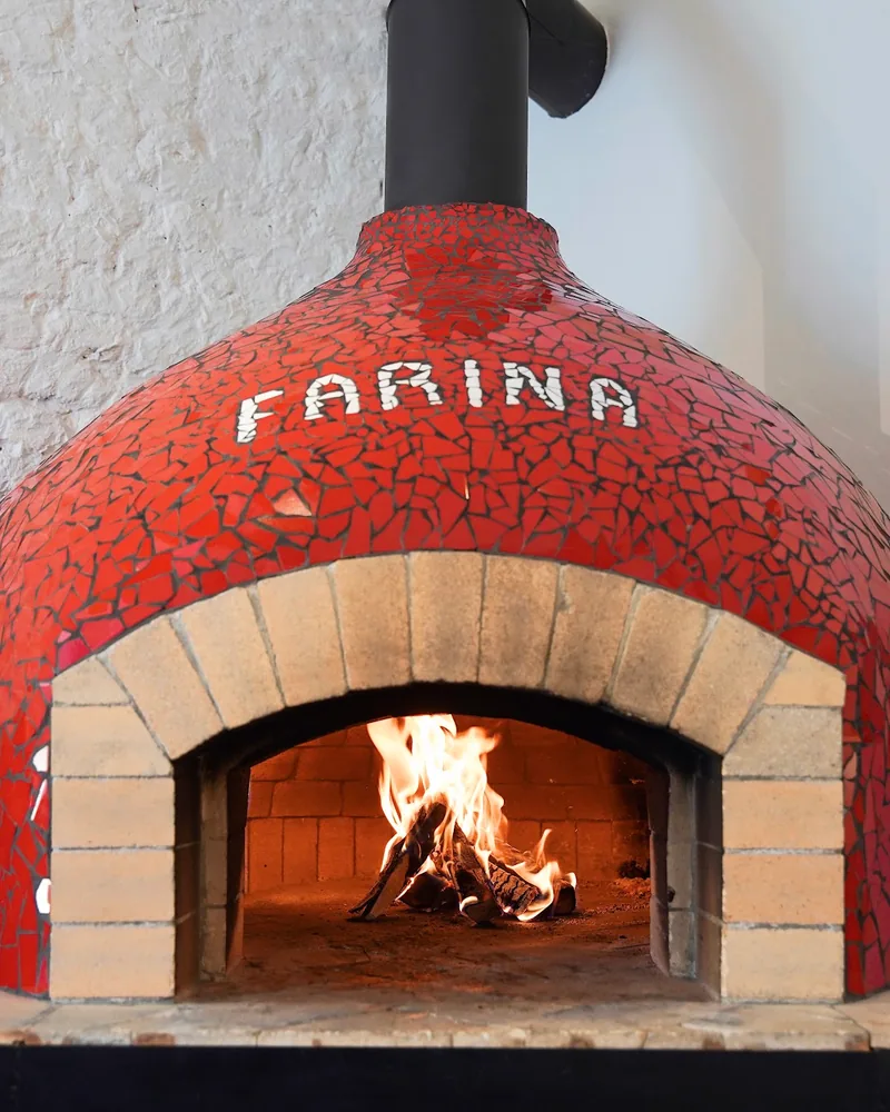 Red mosaic pizza oven with wood fire at Farina