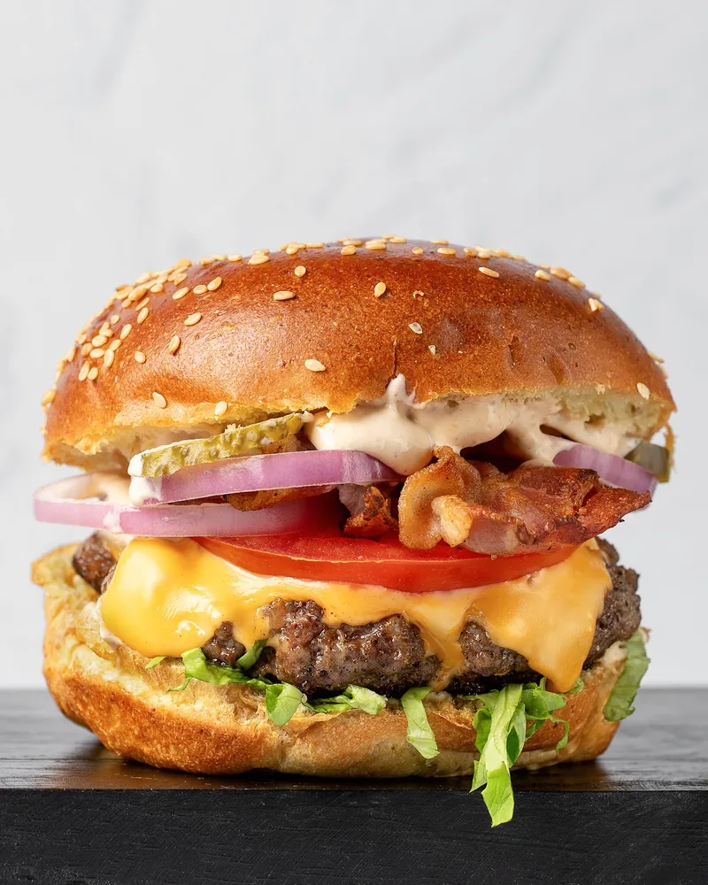 Bacon cheeseburger on a dark wooden surface at Feed Me!