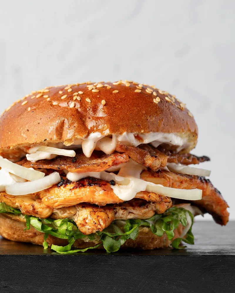 Chicken burger with white sauce on a black surface at Feed Me!
