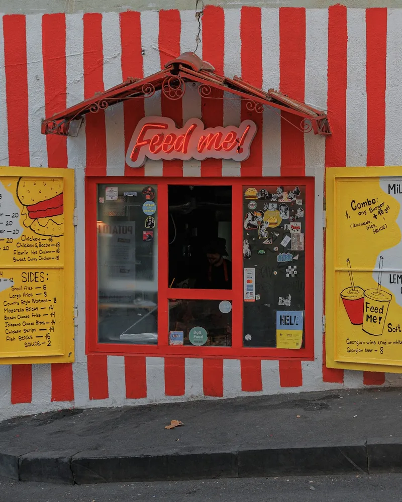 Takeaway hatch with a red and white striped facade and yellow menu shutters at Feed Me!