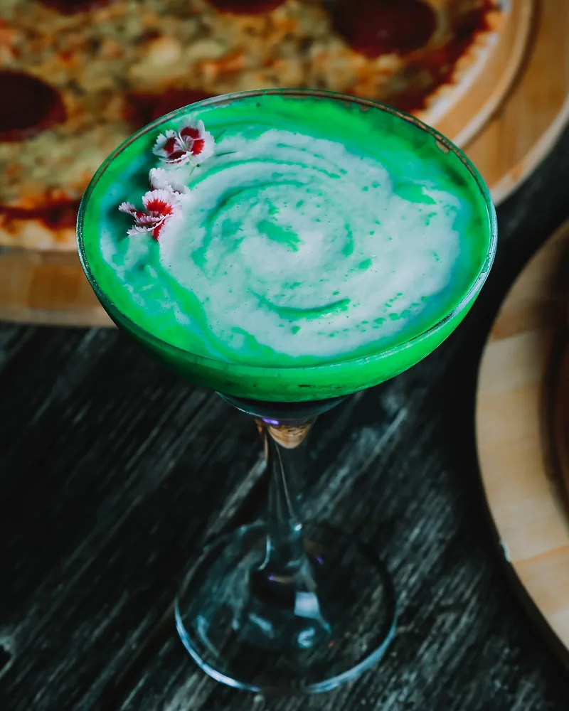 Green cocktail in a coupe glass with a floral garnish at Ficus Bar
