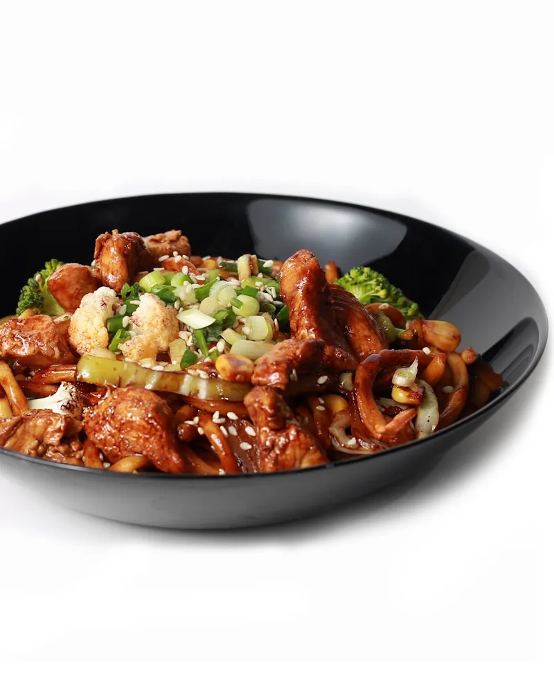 Stir-fried noodles with chicken and vegetables in a black bowl at Fire Wok (Dadiani)