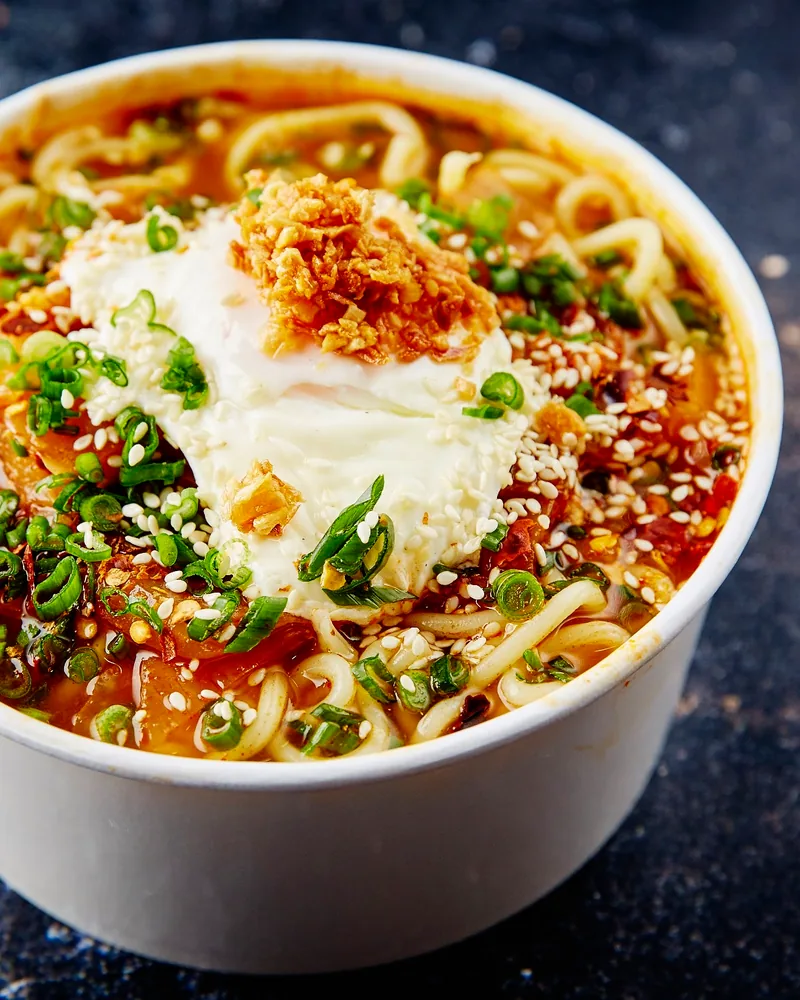 Spicy ramen bowl with poached egg and fried onions in a takeaway cup at Fire Wok (Saburtalo)