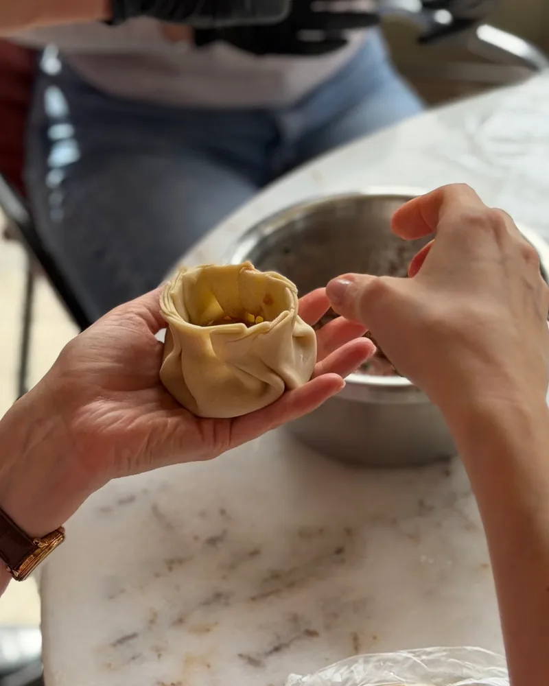 Hands pleating the dough of a raw khinkali around its filling over a marble table at Georgian Cooking Class Tbilisi