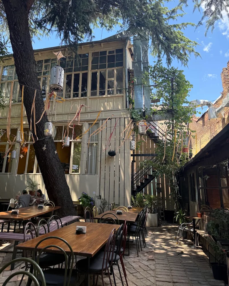 Brick courtyard patio with wooden dining tables under trees at Giorgobistve