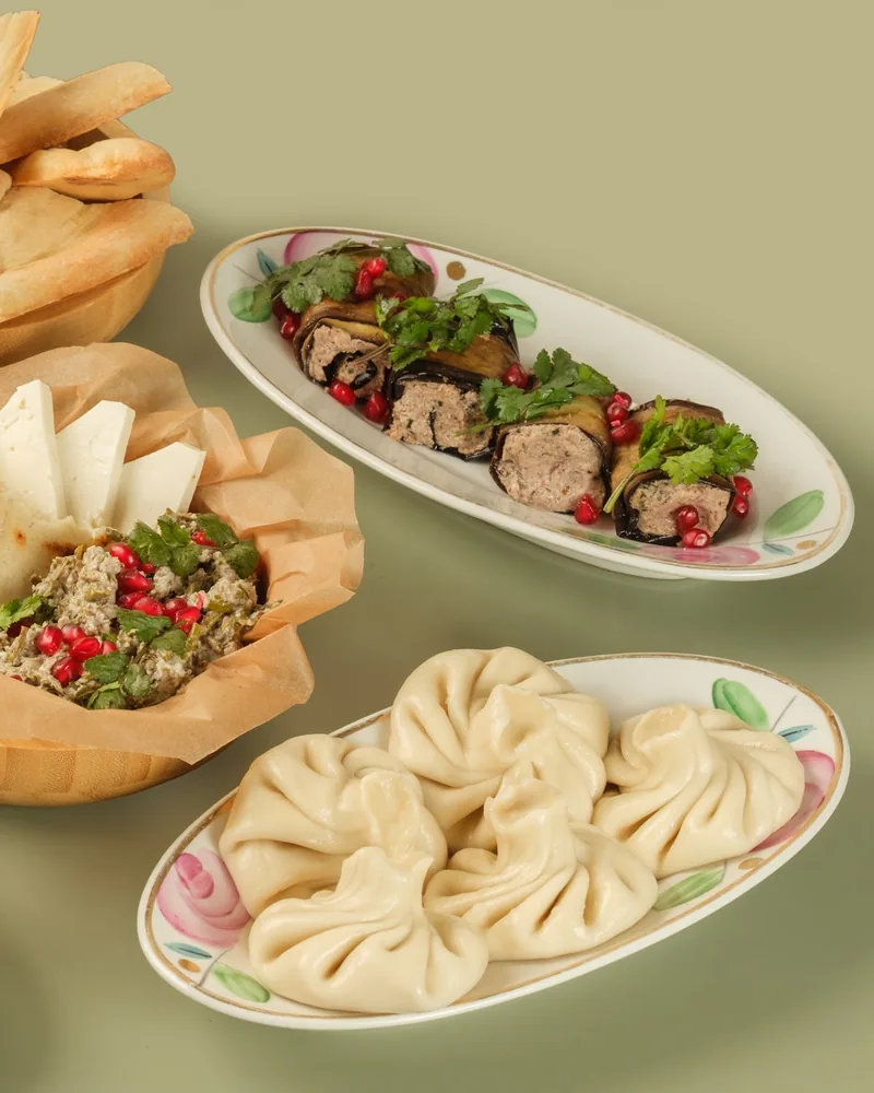 Boiled khinkali, aubergine rolls filled with walnut paste and topped with pomegranate, a chopped herb starter with pomegranate and slices of white cheese, and a bowl of bread