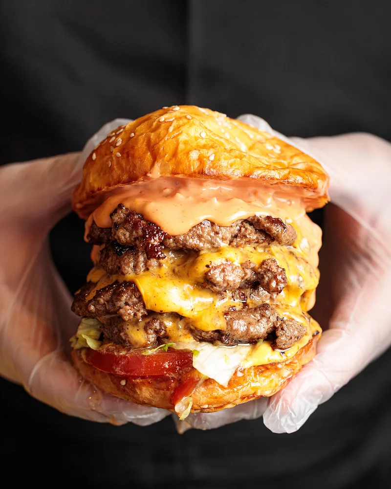 Triple cheeseburger held in gloved hands at Gochits Burger